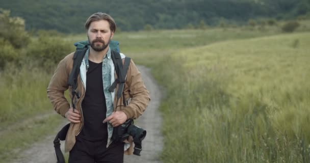 Uomo con zaino e macchina fotografica passeggiando tra il campo verde — Video Stock