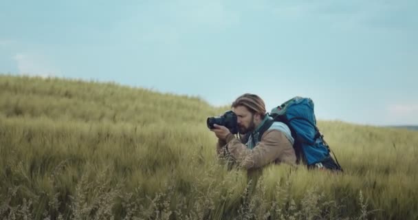 Photographer with backpack taking pictures of green field — Stock Video