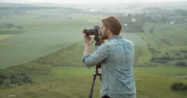 Homem usando tripé e câmera para atirar a natureza da colina — Vídeo de Stock