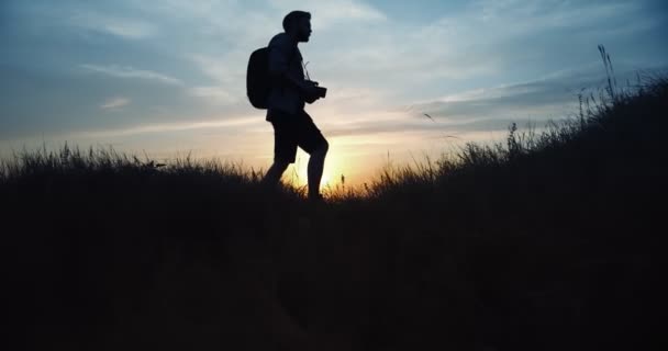 Fotograf in Silhouette geht bei Sonnenuntergang auf einem Hügel spazieren — Stockvideo