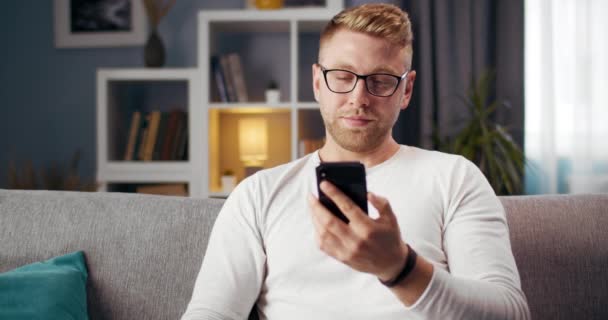 Γενειοφόρος άνθρωπος χρησιμοποιώντας smartphone, ενώ κάθεται στον καναπέ — Αρχείο Βίντεο