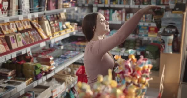 Hermosa chica leyendo el contenido del producto mientras hace compras — Vídeos de Stock