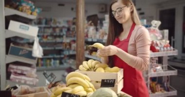 Kadın asistan süpermarkette taze muz düzenliyor.
