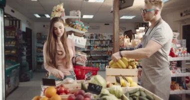 Mağaza çalışanı muz düzenliyor ve müşteriyle konuşuyor.