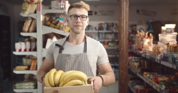 在围裙里微笑的男人在商店里拿着一盒香蕉 — 图库视频影像
