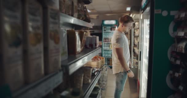 Hombre guapo tomando agua lata de refrigerador en el mercado — Vídeo de stock