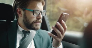 Takım elbiseli adam arabada otururken akıllı telefon kullanıyor.