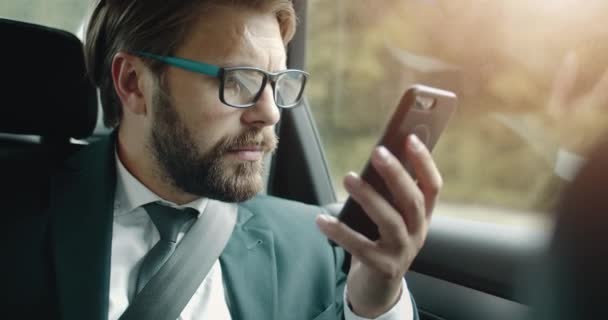 Homem confiante em terno usando smartphone enquanto sentado no carro — Vídeo de Stock