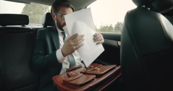 Hombre guapo sentado en el asiento trasero del coche y leyendo documentos — Vídeos de Stock