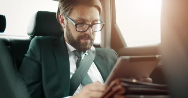 Jóképű üzletember szemüvegben digitális táblagéppel az autóban — Stock videók