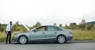 Motoru kontrol etmek için bozuk arabanın kaputunu açan adam.