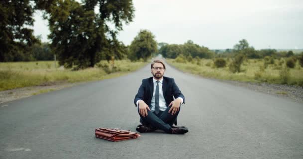 Entspannter Mann im Business-Anzug sitzt in Pose Lotus auf der Straße — Stockvideo