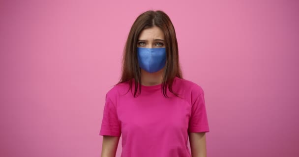 Девушка в медицинской маске смотрит в камеру с грустными эмоциями — стоковое видео