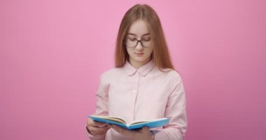 Gözlüklü güzel kadın pembe arka planda kitap okuyor.