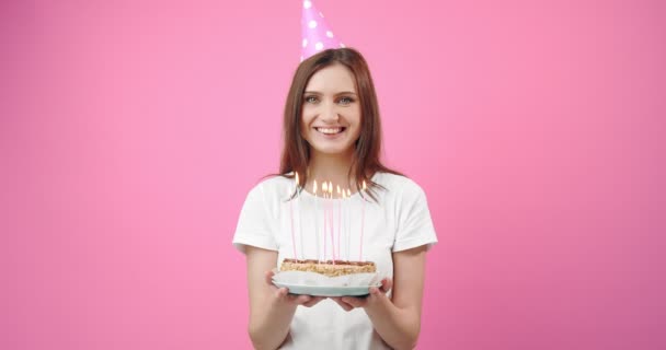 Gelukkig meisje in verjaardag cap holding cake met brandende kaarsen — Stockvideo