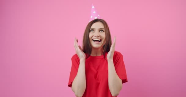 Улыбающаяся девушка в праздничной кепке играет с конфетти в студии — стоковое видео