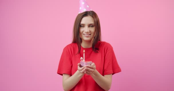 Menina feliz no boné de aniversário soprando vela ardente no bolo — Vídeo de Stock