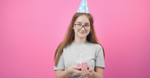 Chica sonriente en gorra de cumpleaños sosteniendo pastel con vela — Vídeos de Stock