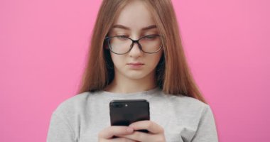 Stüdyoda poz verirken akıllı telefon kullanan gözlüklü kadın.