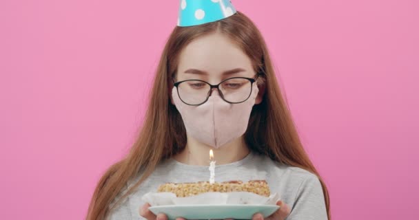 Разочарованная девушка в медицинской маске держит торт на день рождения — стоковое видео