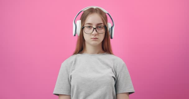 Menina triste em fones de ouvido ouvir música sobre fundo rosa — Vídeo de Stock