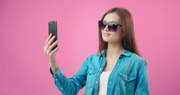 Menina feliz usando smartphone para tirar selfie em estúdio — Vídeo de Stock