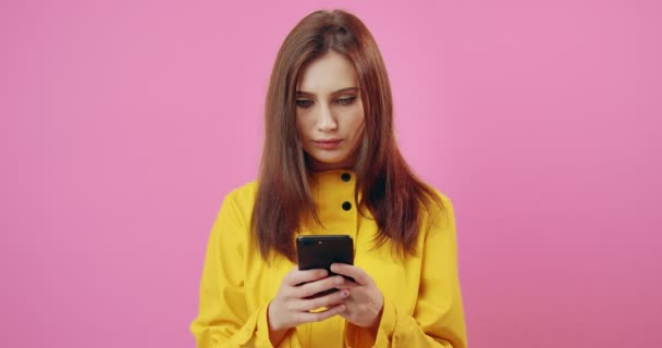 Дівчина в жовтому плащі, використовуючи мобільний на рожевому фоні — стокове відео