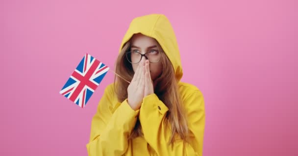 Chica en impermeable amarillo sosteniendo bandera británica en el estudio — Vídeos de Stock