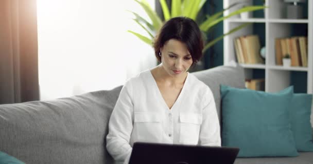 Γοητευτική κυρία με λευκό πουκάμισο που χρησιμοποιεί ασύρματο φορητό υπολογιστή στο σπίτι — Αρχείο Βίντεο