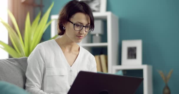 Selbstbewusste Frau in Brille mit tragbarem Laptop auf der Couch — Stockvideo