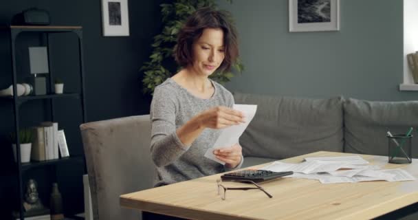 Felnőtt nő ül a nappaliban és számolgatja a számlákat — Stock videók