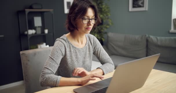 Donna attraente in occhiali da vista che lavorano sul computer portatile a casa — Video Stock