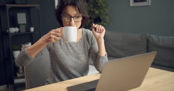 Mutlu kadın kahve içiyor ve dizüstü bilgisayardan film izliyor. — Stok video