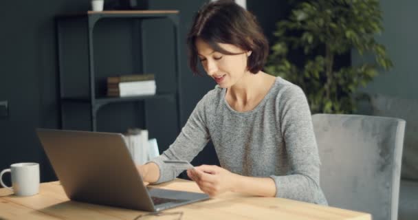 Счастливая женщина использует ноутбук и кредитную карту для интернет-покупок — стоковое видео