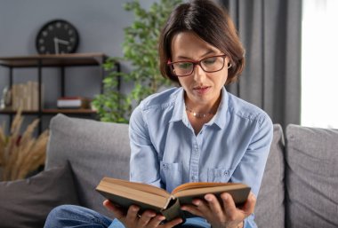 Evde kitap okuyan gözlüklü bir kadın.