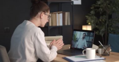 Masada dizüstü bilgisayarlı bir kadın oturuyor ve video görüşmesi yapıyor.