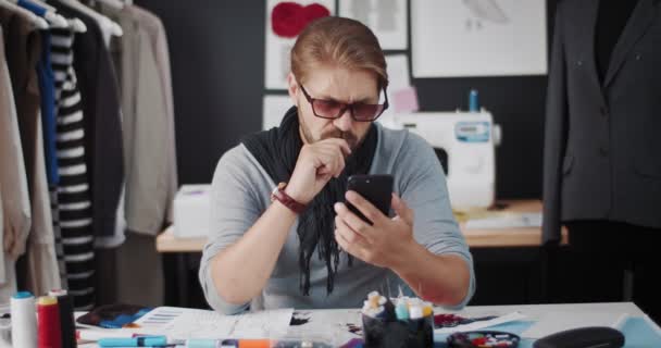 Diseñador barbudo sentado en la mesa y usando un teléfono inteligente — Vídeo de stock