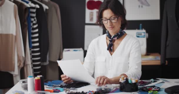 Charmante ontwerper zittend in de kleermakersstudio en schetsen — Stockvideo