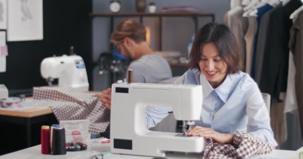 Feliz pareja de diseñadores trabajando en máquinas de coser en atelier — Vídeos de Stock