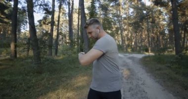 Yeşil ormanda ısınan spor elbiseli güçlü bir adam.