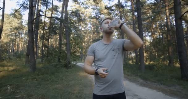 Muskularny mężczyzna pijący wodę po treningu w lesie — Wideo stockowe