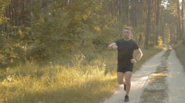 Yeşil ormanda koşan spor kıyafetli kaslı adam.