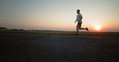 Gün batımında asfalt yolda koşan yakışıklı adam.