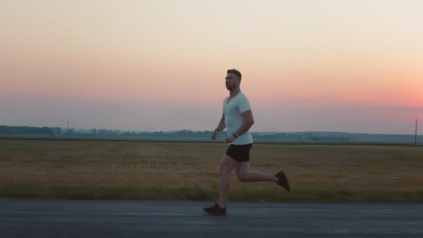 Strong muscular jogging on asphalt road during sunset — Stock Video