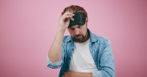 Barbudo hombre en la máscara del sueño sensación de cansancio sobre fondo rosa — Vídeo de stock