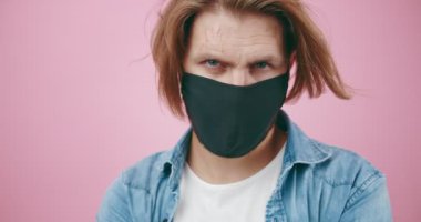 Kamerada poz verirken tıbbi maske takan ciddi bir adam.
