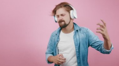 Olgun bir adam pembe arka planda kulaklıkla müzik dinlemekten hoşlanıyor.