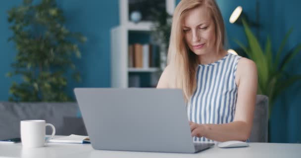 Mujer sentada en la mesa y usando portátil para trabajo remoto — Vídeo de stock