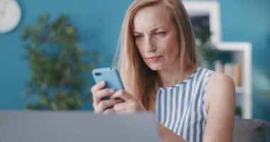 Masada açık dizüstü bilgisayarla otururken cep telefonu kullanan kadın
