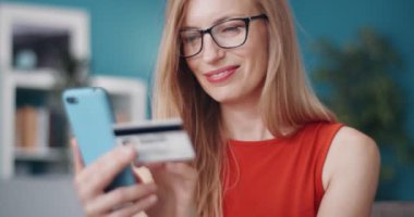 Neşeli bayan cep telefonunda online ödeme için kredi kartı kullanıyor.